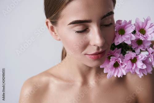 Attractive young woman keeping beautiful pink flowers on naked shoulder