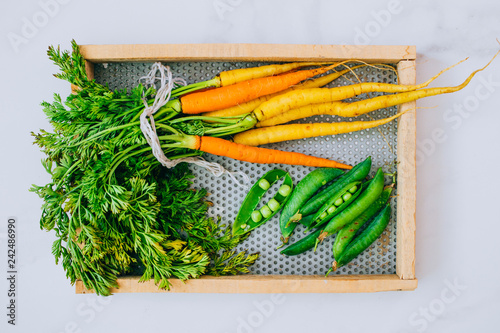 Fresh washed carrots with green peas on wooden tray on a marble background, top view