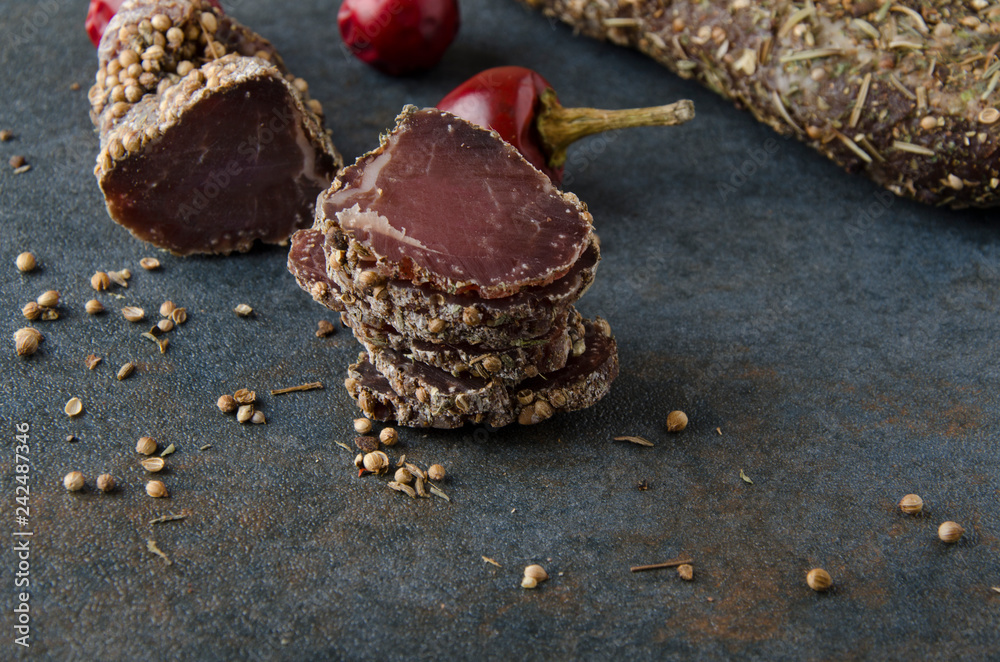 Slices of dried meat with coriander and other spices on grey table Slices of dried meat with coriander and other spices on grey table
