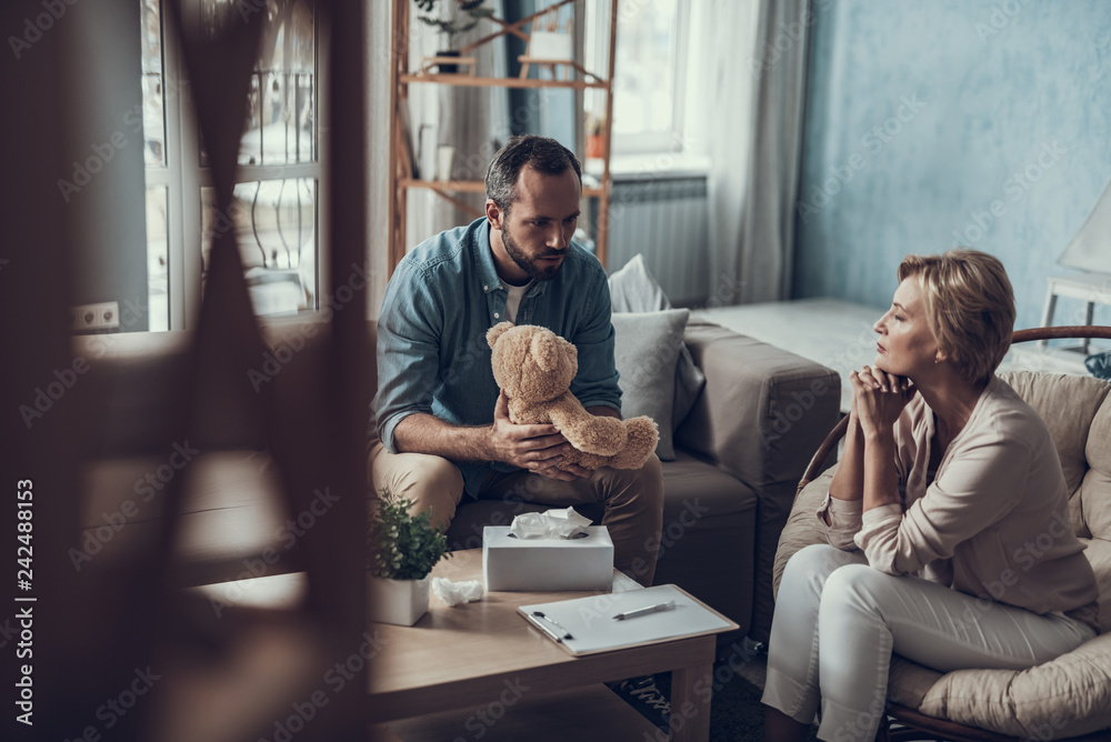 Man with teddy bear looking astonished and psychotherapist looking calm Man with teddy bear looking astonished and psychotherapist looking calm