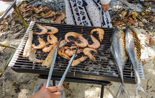 humand hand grilling seafood, crayfish, shrimps and tuna fish at the beach. photo