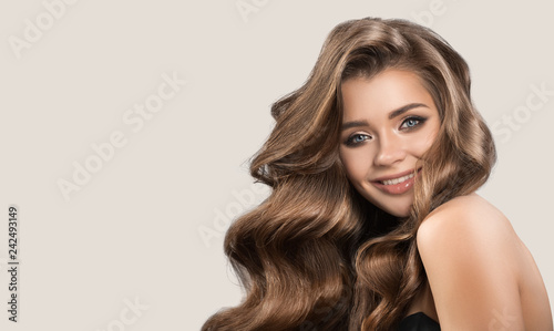 Portrait of beautiful cute woman with curly brown long hair. Gray background.