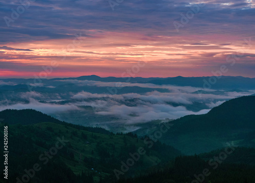 Panoramic photo of Mountain range through the morning colorful fog in the summer. Beautiful sunrise in the Carpathian Mountains with visible silhouettes and pink clouds in the sun rays. © Viktoria