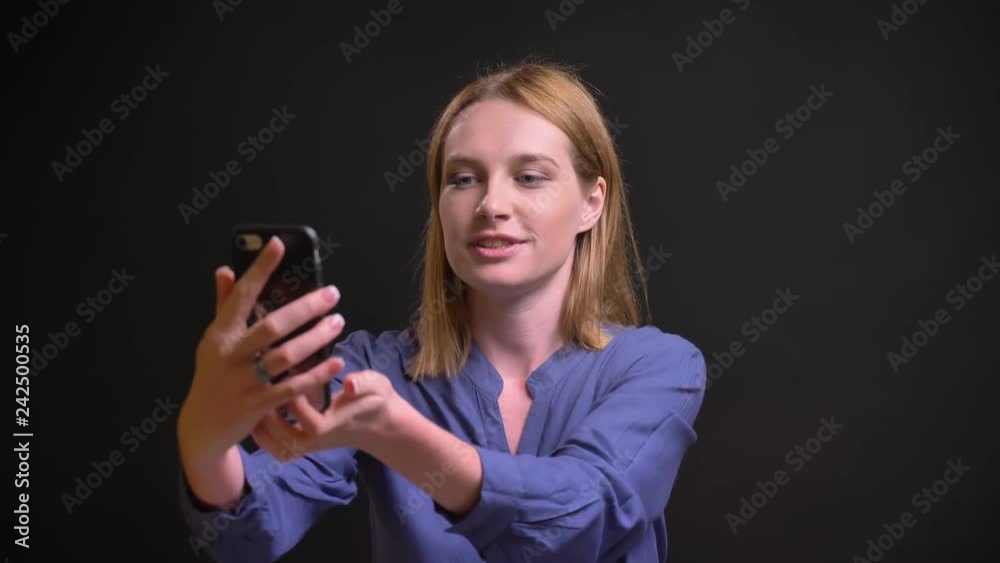 Portrait of caucasian blonde woman in shirt talking in videochat using smartphone on black background. Portrait of caucasian blonde woman in shirt talking in videochat using smartphone on black background.