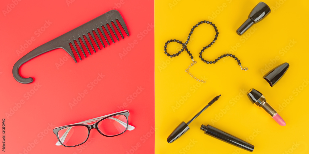 Glasses, cosmetics, jewelry and comb on a yellow and red background. Wide photo.