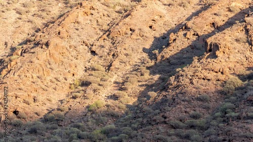 Full frame video footage of the rocky and arid landscape of the volcanic Gran Canaria (Canary Islands) with a slow upward pan following the shadow of the setting time lapse sun.