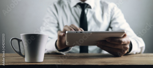Coffee cup on table. Businessman using white digital tablet.