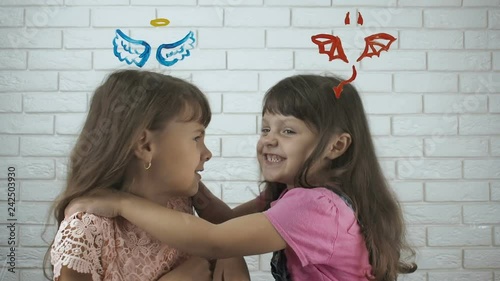 The kids are fighting. Sisters feuding. Angel and demon. Little girls with angel wings and devil horns painted over them. A kind and wicked sister. photo