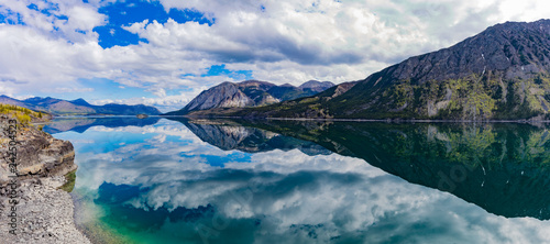 Panoramic view of calm water of Windy Arm of Tagish Lake near Carcross, Yukon Territory, Canada, with surrounding mountains mirrored on lake surface