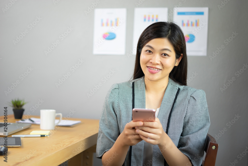 Smiling Business girl working in office with laptop,Happy Asian business woman using phone sitting on a chair at modern home studio.Concept of young people working mobile devices,contact to customer Smiling Business girl working in office with laptop,Happy Asian business woman using phone sitting on a chair at modern home studio.Concept of young people working mobile devices,contact to customer