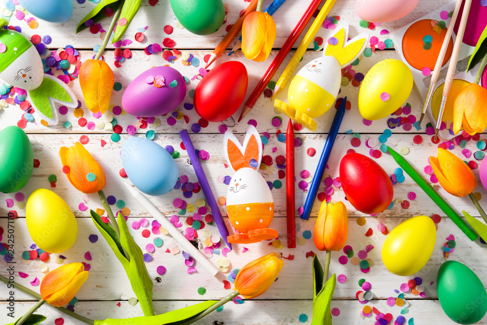 Fototapeta premium Easter background with eggs, tulips and confetti on white wooden background.