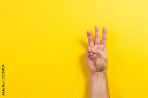 Man hand showing three fingers on yellow background. Number two symbol