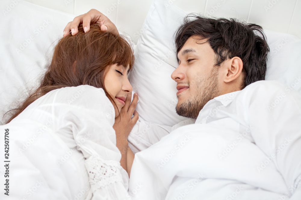 Young couple in love looking at each other lying together on white bed Romantic moment in morning to rub gently on the head Young couple in love looking at each other lying together on white bed Romantic moment in morning to rub gently on the head