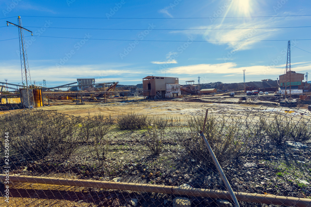 Barbed wire fall of access to the old mining complex of Riotinto, with conveyor belt of mineral and old buildings