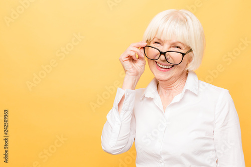 Joyful senior lady in glasses laughing isolated over yellow background. Friendly, mature white haired woman wearing glasses with a smile.