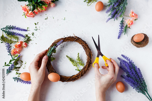 Female hands make Easter wreath of flowers, herbs and eggs on a light background. Easter concept