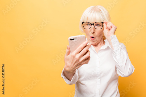 Wow! Phone conversation. Surprised aged woman using phone, isolated over yellow background.