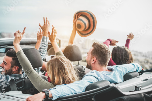 Happy friends with hands up having fun in convertible car on summer vacation