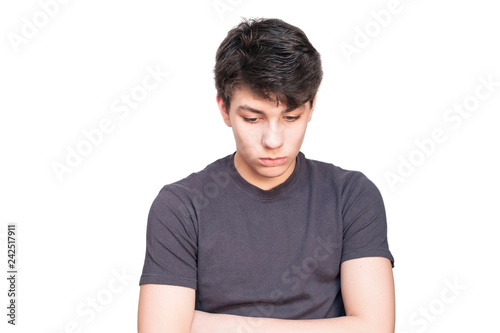 A boy of an adolescent age on a white background with a sad face looks down, hides eyes from people. Isolated