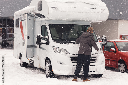 camping car or campervan getting ready in the parking space and man clean it for outdoor journey on the mountain side in the snow