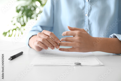 Young woman slipping ring off her finger at table, closeup. Concept of divorce photo