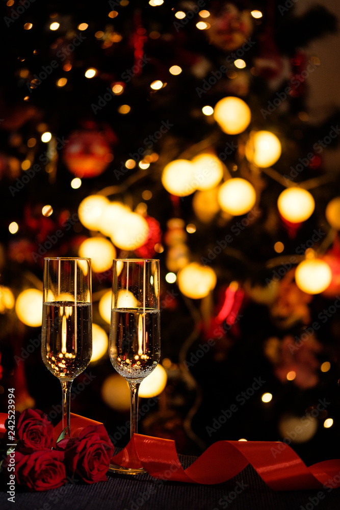 Glasses of champagne on the background of lights with roses and red ribbon Glasses of champagne on the background of lights with roses and red ribbon