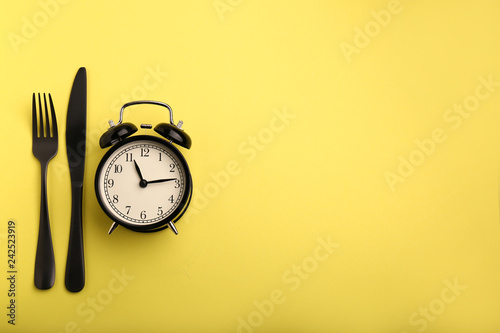 Alarm clock and cutlery on color background. Diet concept photo