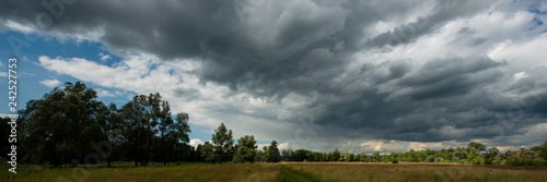 Thunderclouds over forest and meadow in the countryside. Web banner.