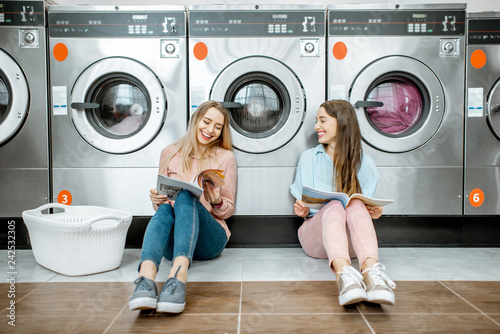 Fotografija Two cheerful girlfriends having fun together while waiting for the clothes washi