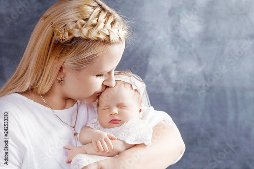 Pretty woman holding a newborn baby girl in her arms. Happy mother kissing her slipping newborn baby. Happy family concept. Close up picture.