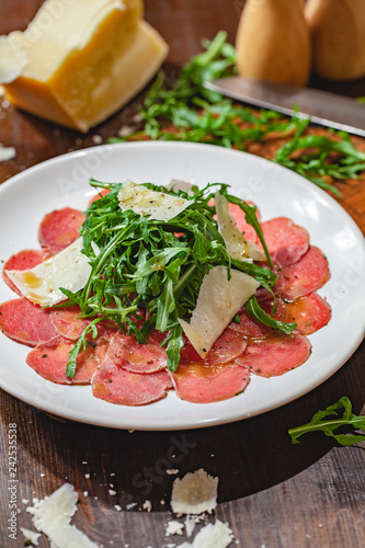 Meat carpaccio with arugula and parmesan cheese on white plate. Close up