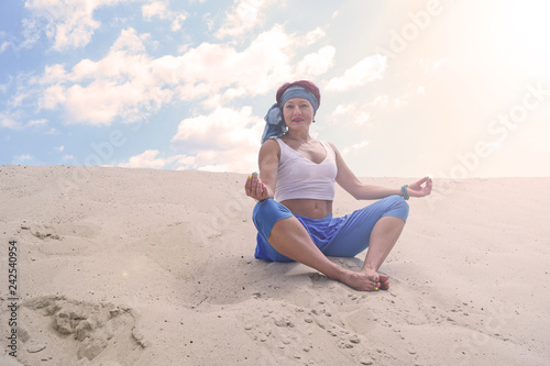An old woman sitting on the sand in the desert in a Lotus position. Yoga, exercise.