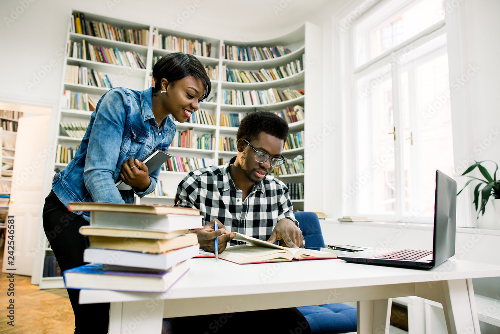 Male and female african students studying together for finals. Happy young university students studying with laptop in college library sitting together at table with books and laptop. Male and female african students studying together for finals. Happy young university students studying with laptop in college library sitting together at table with books and laptop.