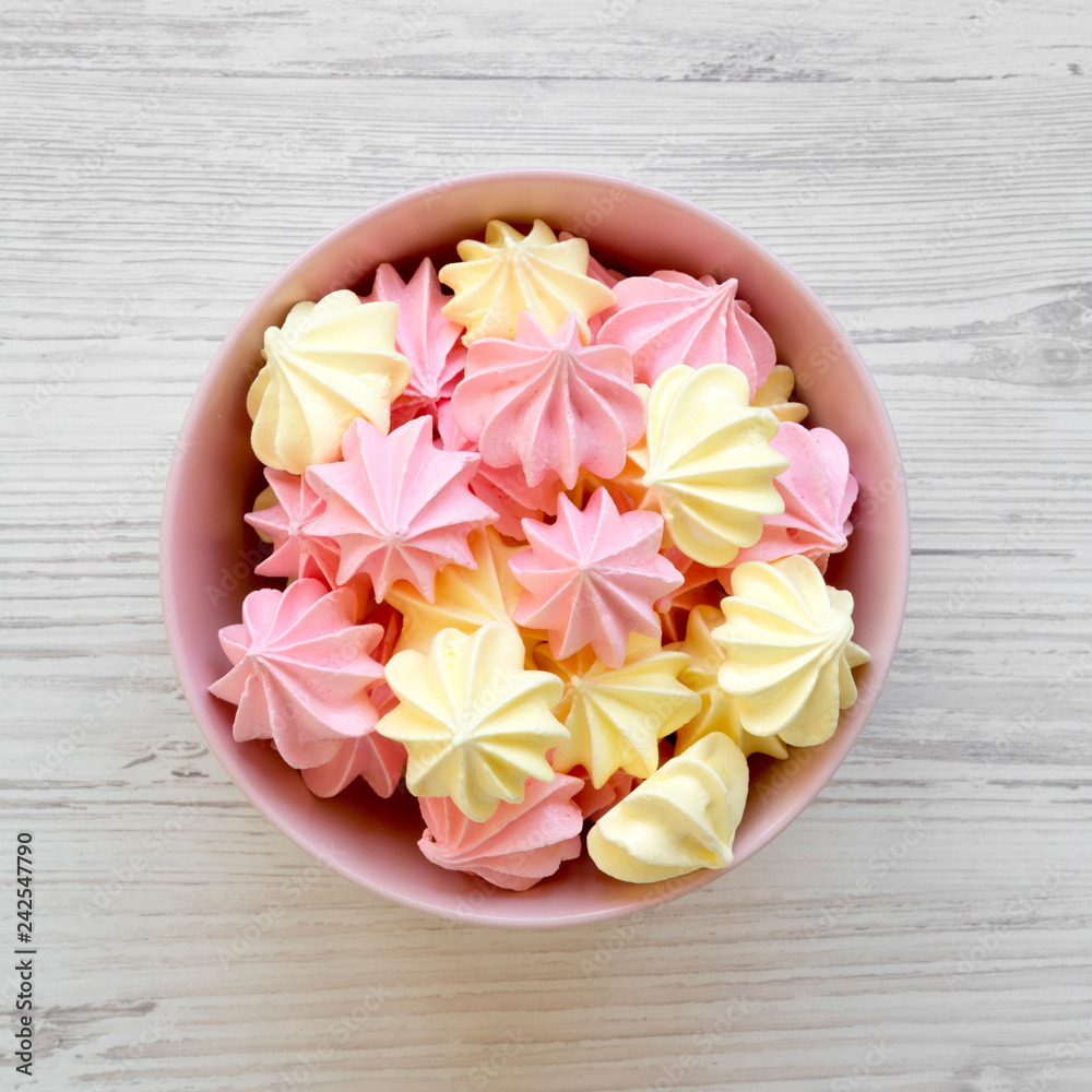 Mini meringues in a pink bowl over white wooden table, top view. From above, overhead. Mini meringues in a pink bowl over white wooden table, top view. From above, overhead.
