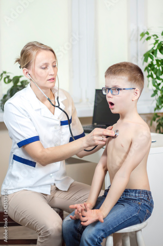 Chłopiec podczas badania stetoskopem przez lekarza pediatrę głęboko oddycha przez otwarte usta.