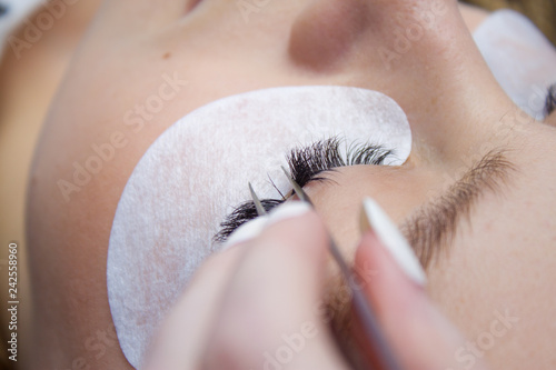 Eyelash Extension Procedure. Woman Eye with Long false Eyelashes. Close up macro shot of tweezers in hands of beautican. photo