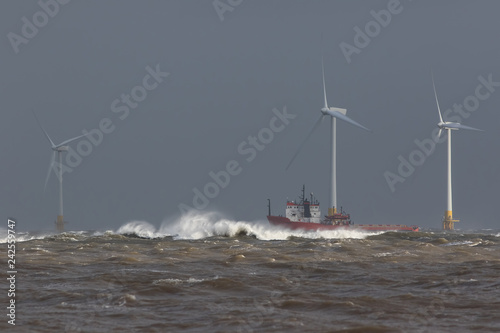 Ship sailing in rough sea around offshore wind farm turbines.