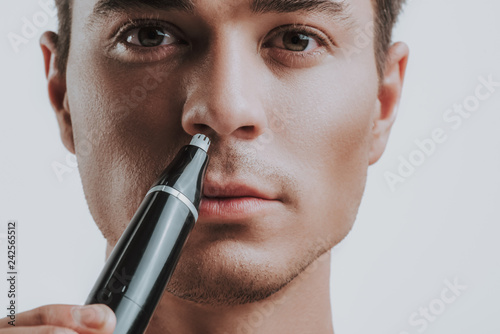 Close up of calm man using modern nose trimmer photo