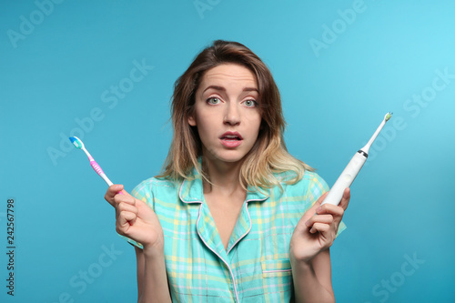 Fototapeta Naklejka Na Ścianę i Meble -  Young woman choosing between manual and electric toothbrushes on color background