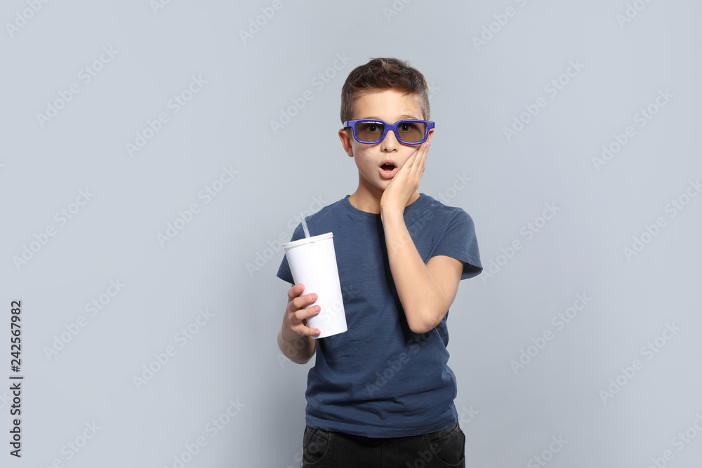 Fototapeta premium Emotional boy with 3D glasses and beverage during cinema show on grey background