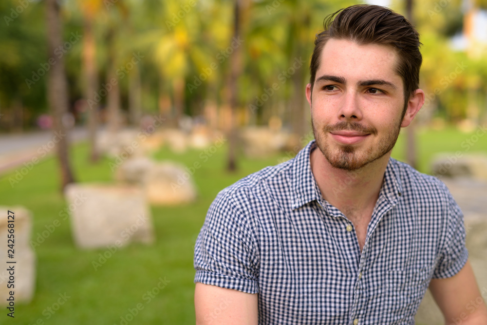 Portrait of young handsome man sitting at park while thinking Portrait of young handsome man sitting at park while thinking