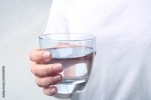 Woman holding glass with fresh water against light background, closeup