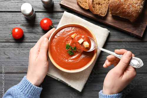 Woman eating fresh homemade tomato soup at wooden table, top view