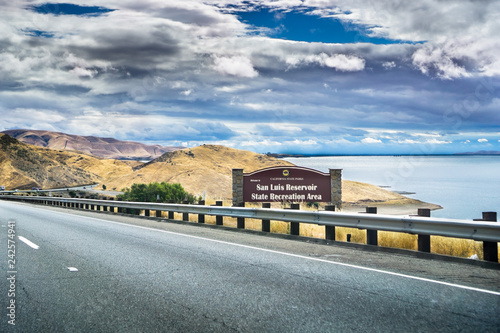 Driving through the golden hills of California; the San Luis Reservoir State Recreation area sign and dam on the right side of the road; photo