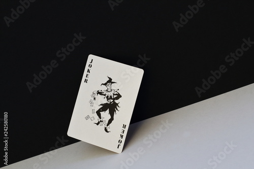 Unpredictable joker as symbol of opposites, contradictions of human nature. Black joker on contrasting white and black background.