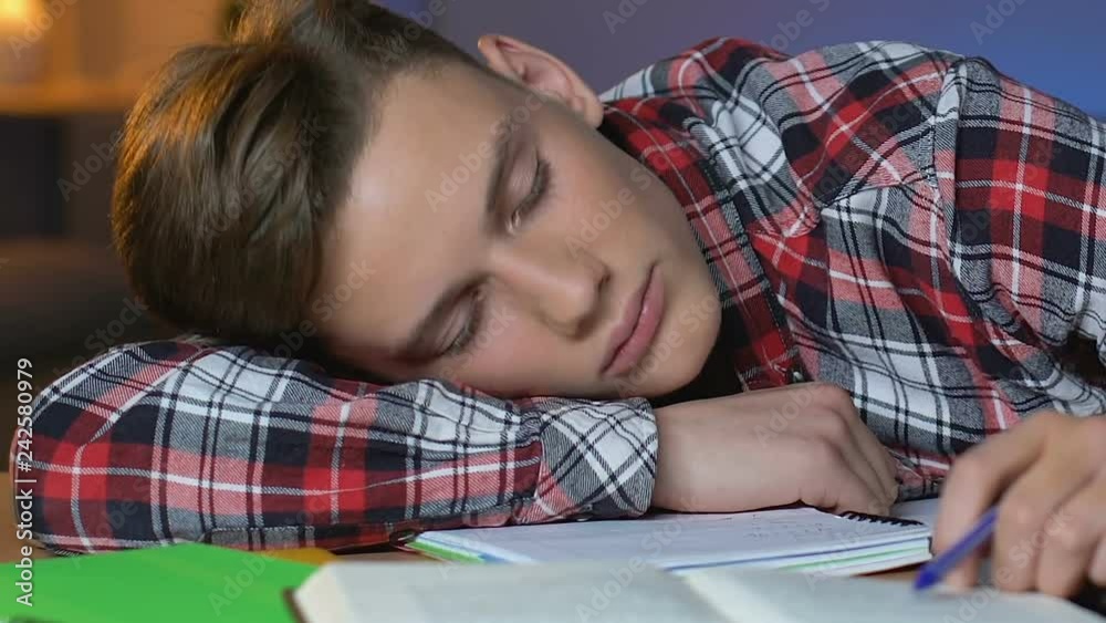 Tired schoolboy sleeping on table, preparation for exam, overworked student Tired schoolboy sleeping on table, preparation for exam, overworked student