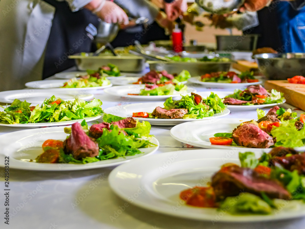 Cooked Roast Beef, Fresh Salad And Tomatoes Served On White Plates. Cooking Master Class, Workshop with People Learning How to Cook Around the Table. Cooked Roast Beef, Fresh Salad And Tomatoes Served On White Plates. Cooking Master Class, Workshop with People Learning How to Cook Around the Table.