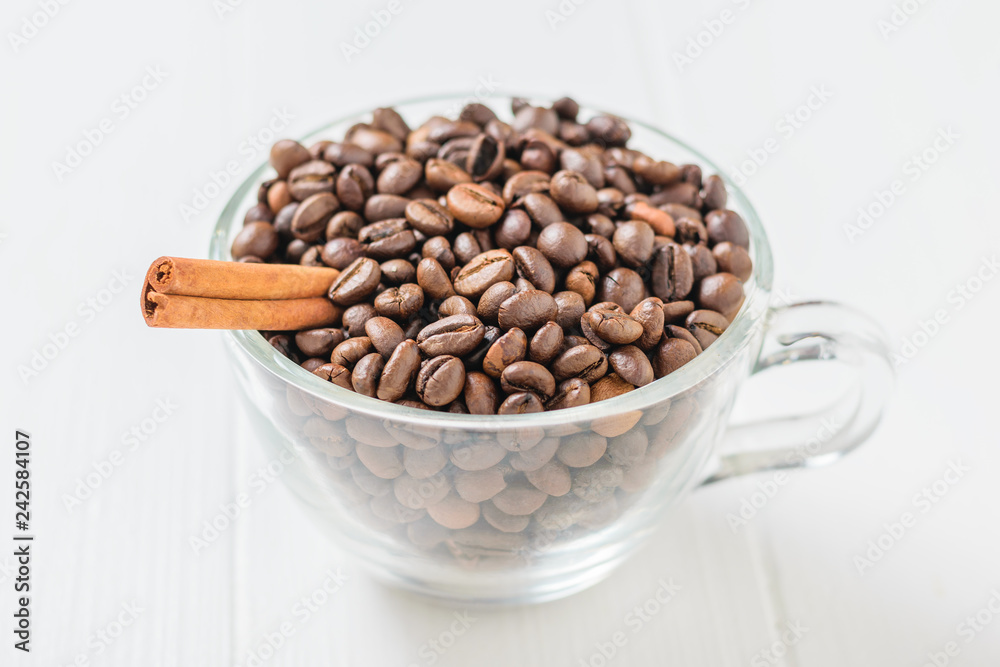 Fototapeta premium Glass bowl with coffee beans and cinnamon stick on white rustic table.