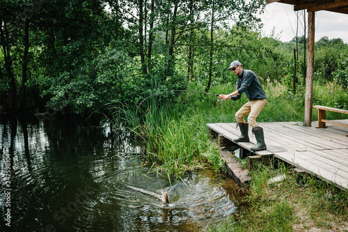 Fisherman with fishing rod caught a big fish pike out of water on bridge, pier. Good catch. Trophy fish. angler. Fishing background, grass, trees against the backdrop of lakes, river. wild nature.