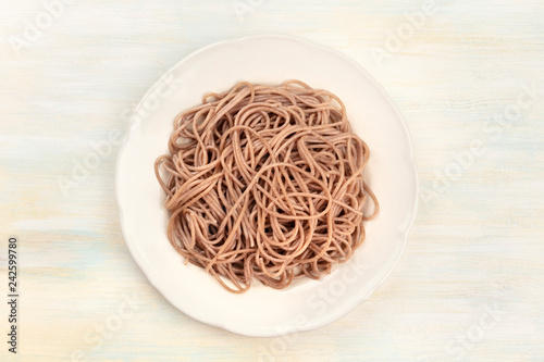 A plate of soba, buckwheat noodles, shot from above on a pale wooden background with a place for text